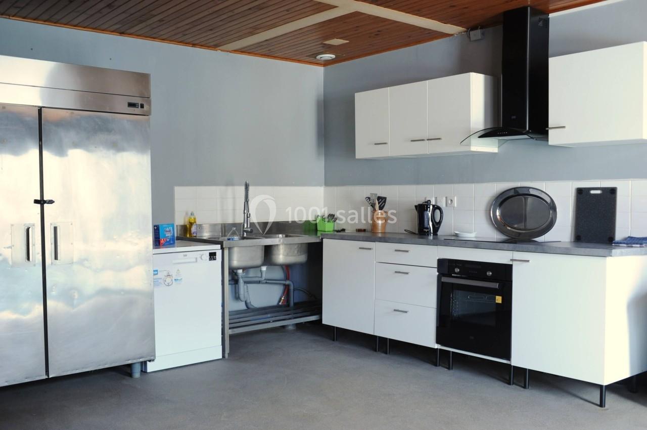 Cuisine moderne avec réfrigérateur en acier inoxydable, évier double, plaques de cuisson, four et rangements blancs.