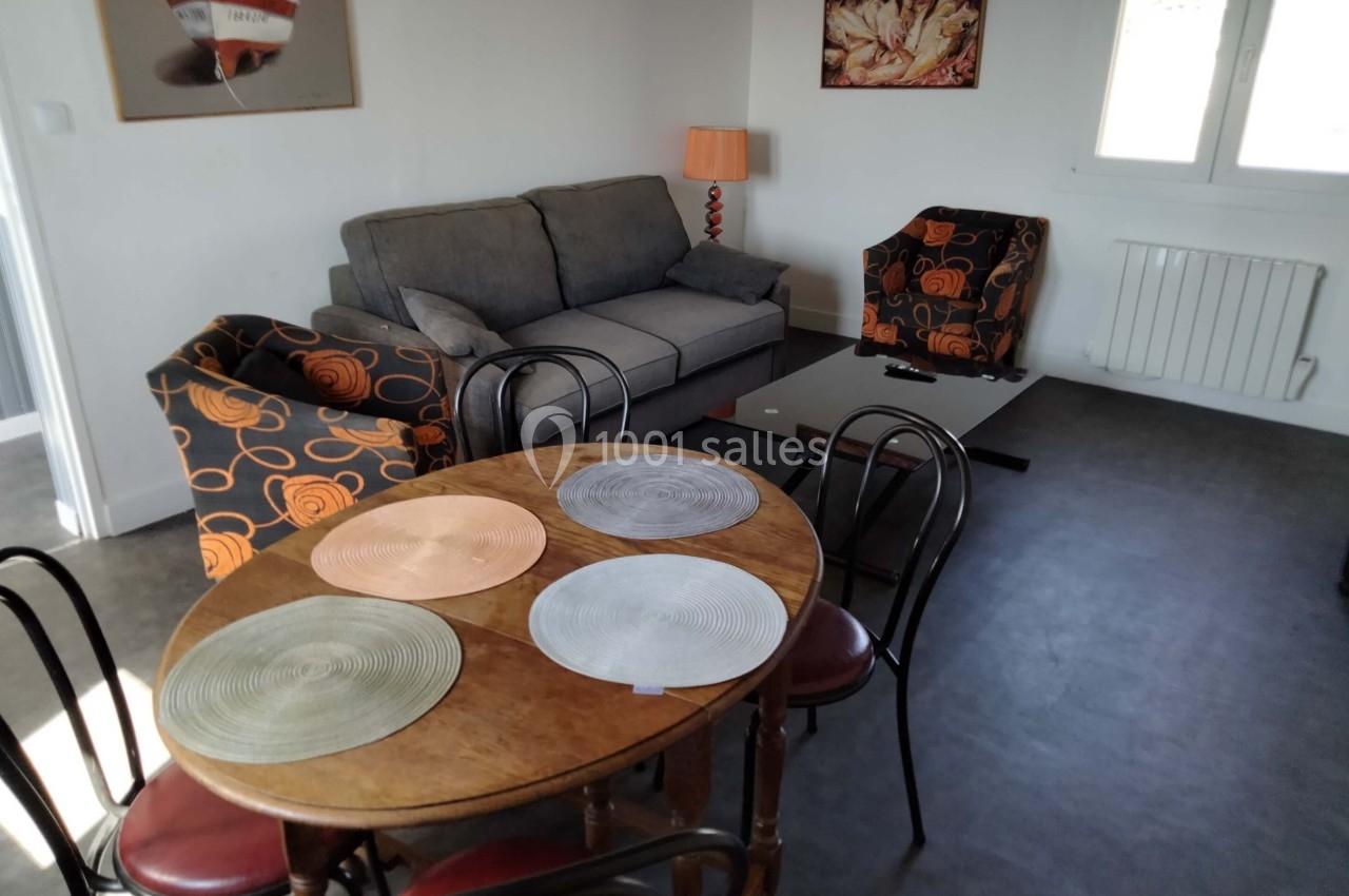 Salon avec canapé gris, fauteuils à motifs orange, table ronde en bois avec sets de table et lampe sur pied.