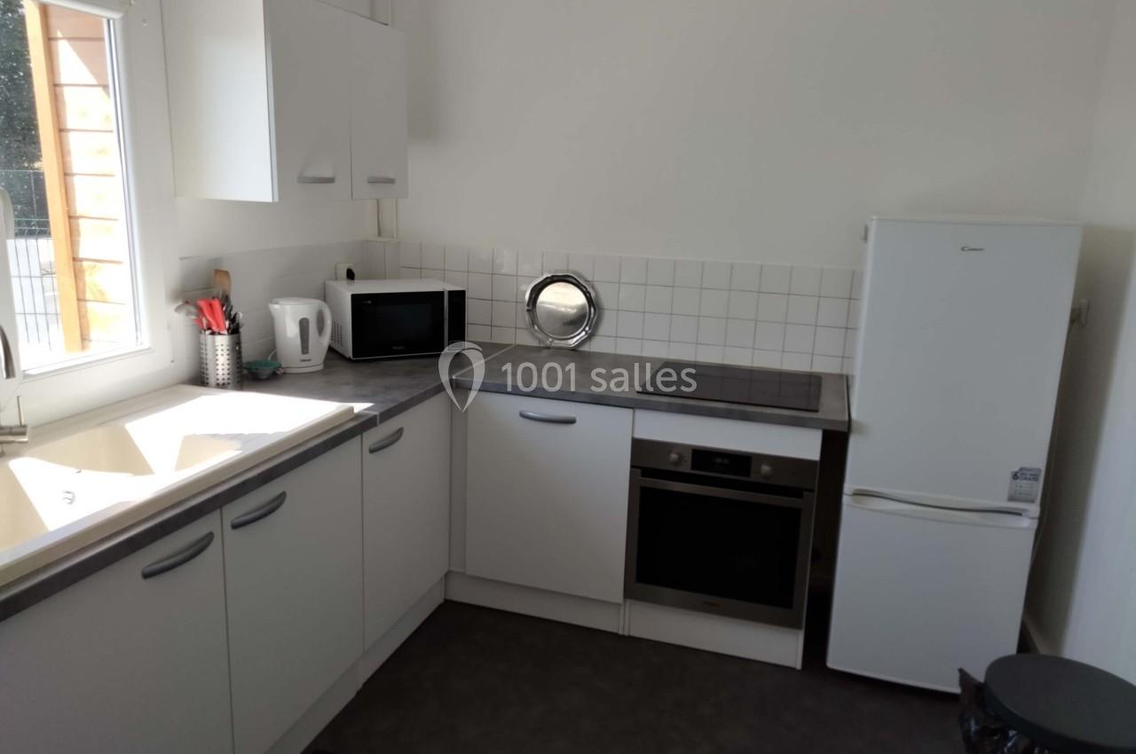 Cuisine moderne avec meubles blancs, évier, plaques de cuisson, four, micro-ondes, réfrigérateur et lumière naturelle.