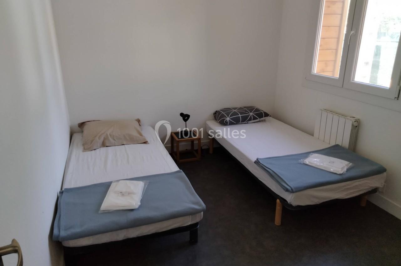 Deux lits simples avec draps pliés, une table de chevet et une fenêtre laissant entrer la lumière naturelle.