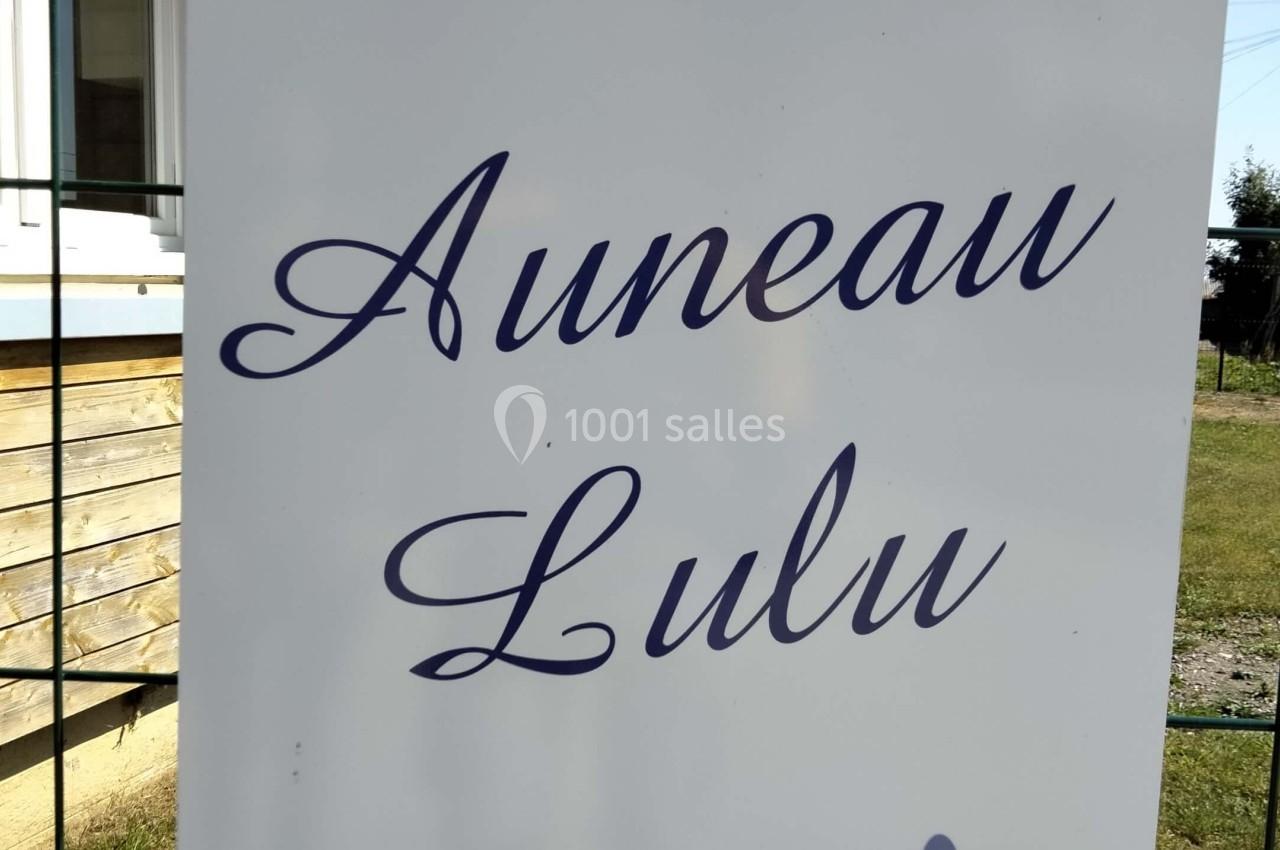 Panneau blanc avec les inscriptions ’Auneau Lulu’ en lettres bleues, décoré de motifs floraux, fixé à un grillage.