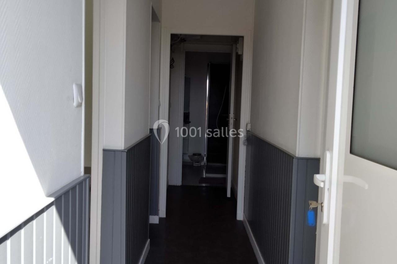 Couloir étroit avec murs blancs et gris, sol sombre, portes ouvertes et vue sur une salle de bain au fond.