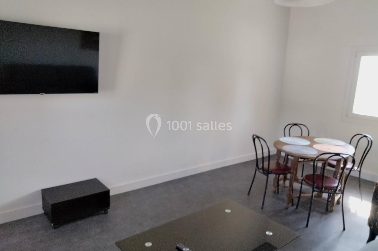 Salle avec un téléviseur mural, une table ronde entourée de chaises et une table basse noire.