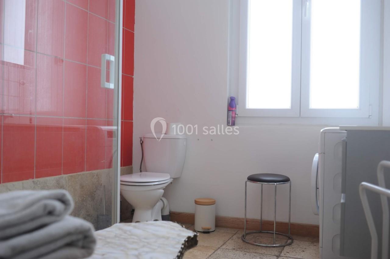 Salle de bain lumineuse avec toilettes, douche à paroi rouge, fenêtre, tabouret et machine à laver.