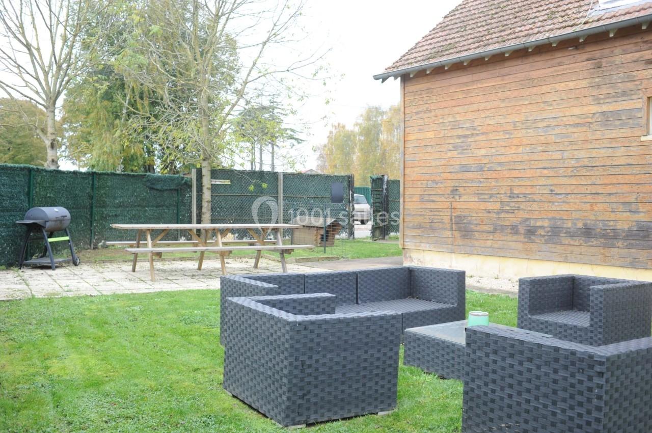 Mobilier de jardin en résine tressée sur une pelouse, avec une table de pique-nique et un barbecue en arrière-plan.