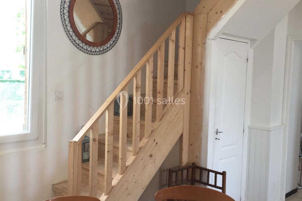 Escalier en bois clair dans un intérieur lumineux, avec une table ronde et un miroir mural circulaire.
