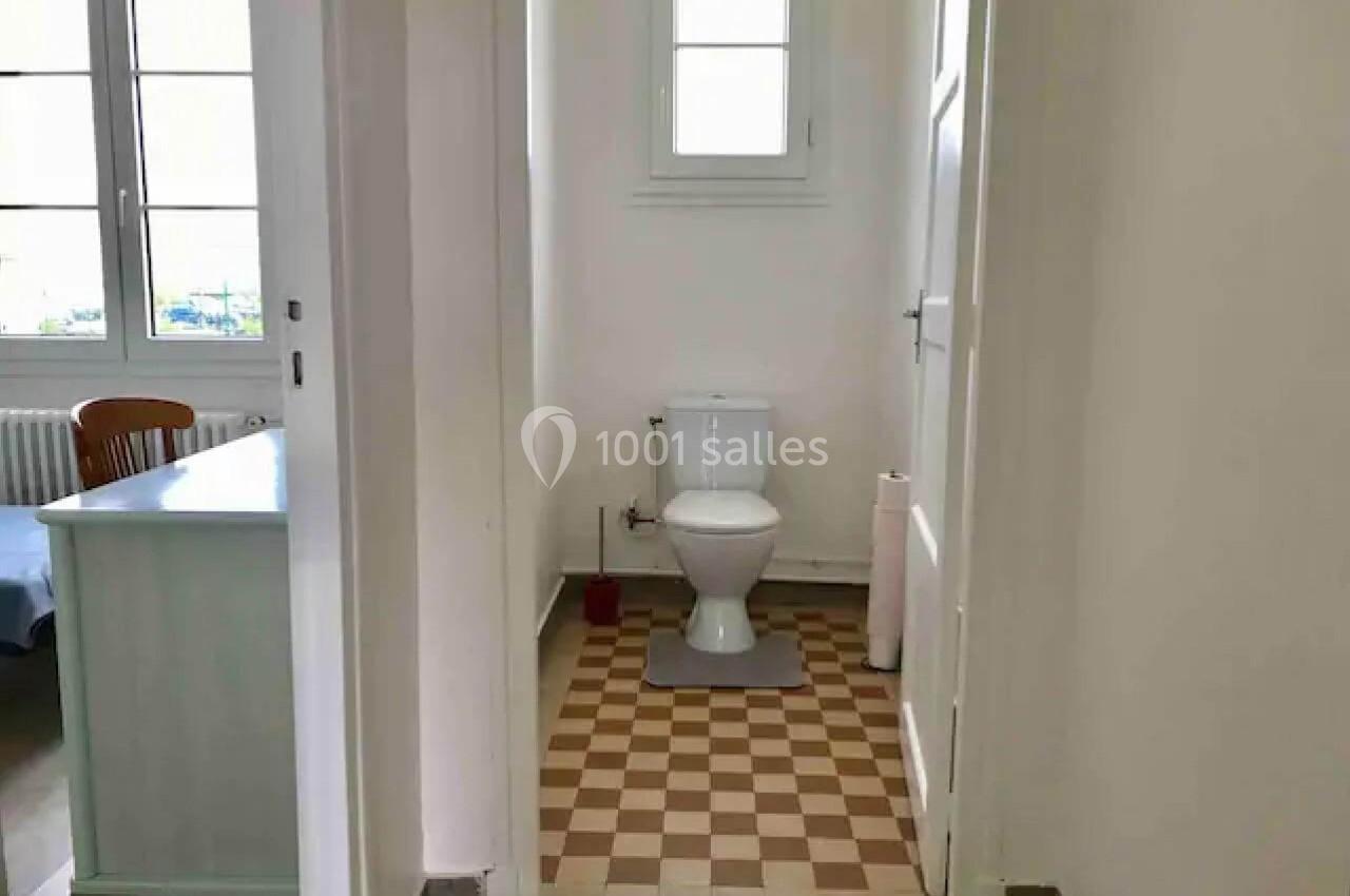 Toilettes dans une petite pièce lumineuse avec carrelage à motifs, situées près d'une fenêtre et d'un bureau.