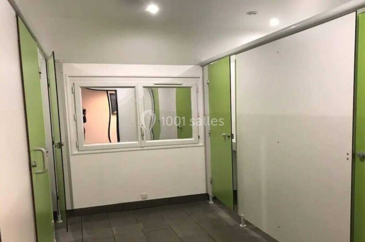 Cabines de toilettes avec portes vertes et murs blancs, éclairées par des lumières au plafond.