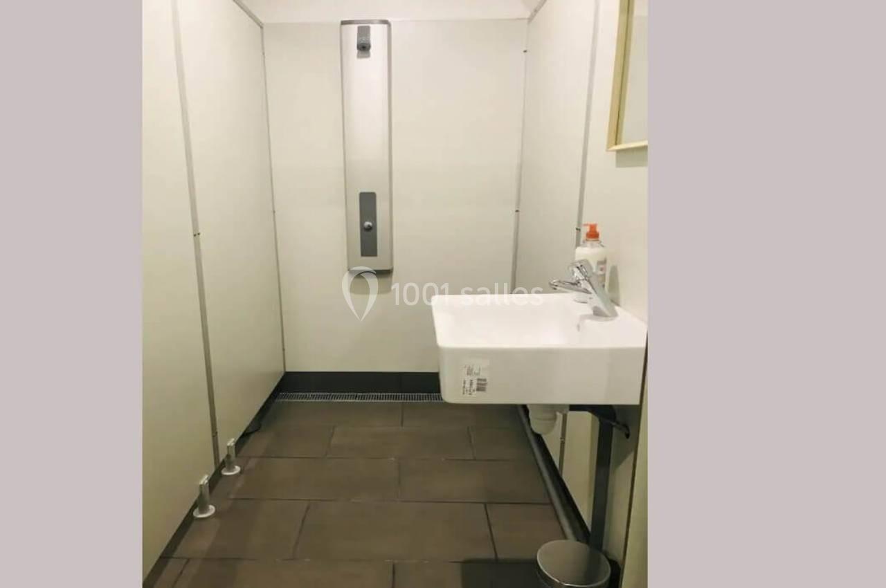 Toilettes avec un lavabo mural, un distributeur de savon, un miroir et des cloisons séparatives.