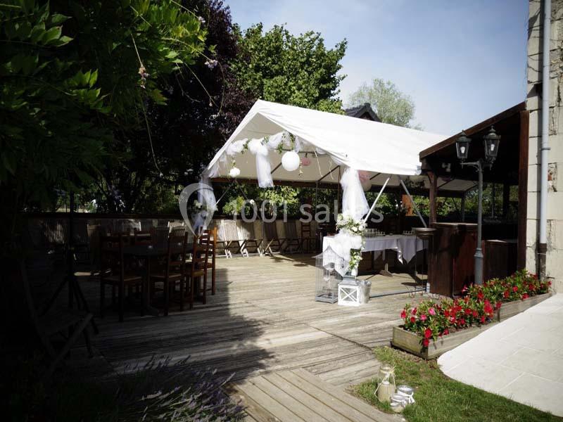 Tente blanche décorée pour un événement sur une terrasse en bois, entourée de verdure et de fleurs.