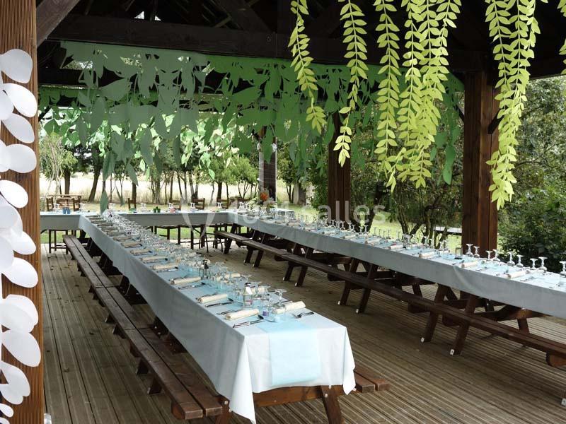 Tables longues dressées avec nappes bleues sous une pergola décorée de feuillages suspendus.