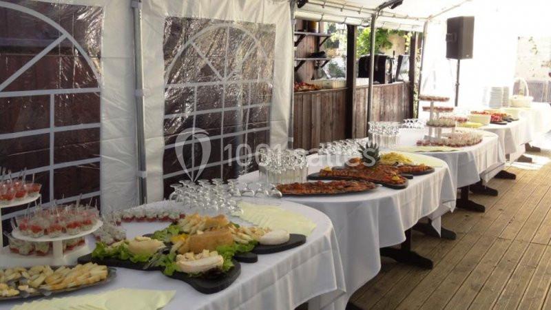 Buffet en extérieur sous une tente, avec des tables garnies de plats variés, verrines et assiettes prêtes à servir.