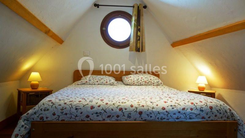 Lit double avec une couette à motifs floraux dans une chambre mansardée, éclairée par deux lampes de chevet et une fenêtre…