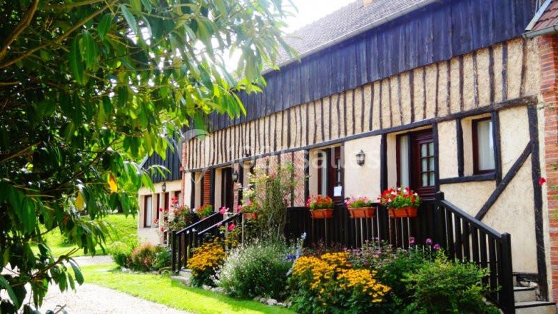 Façade d'une maison à colombages avec jardinières fleuries et un jardin verdoyant au premier plan.