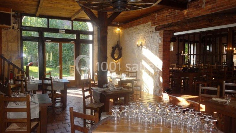 Salle de restaurant rustique avec tables en bois, grandes fenêtres donnant sur un jardin et lumière naturelle abondante.