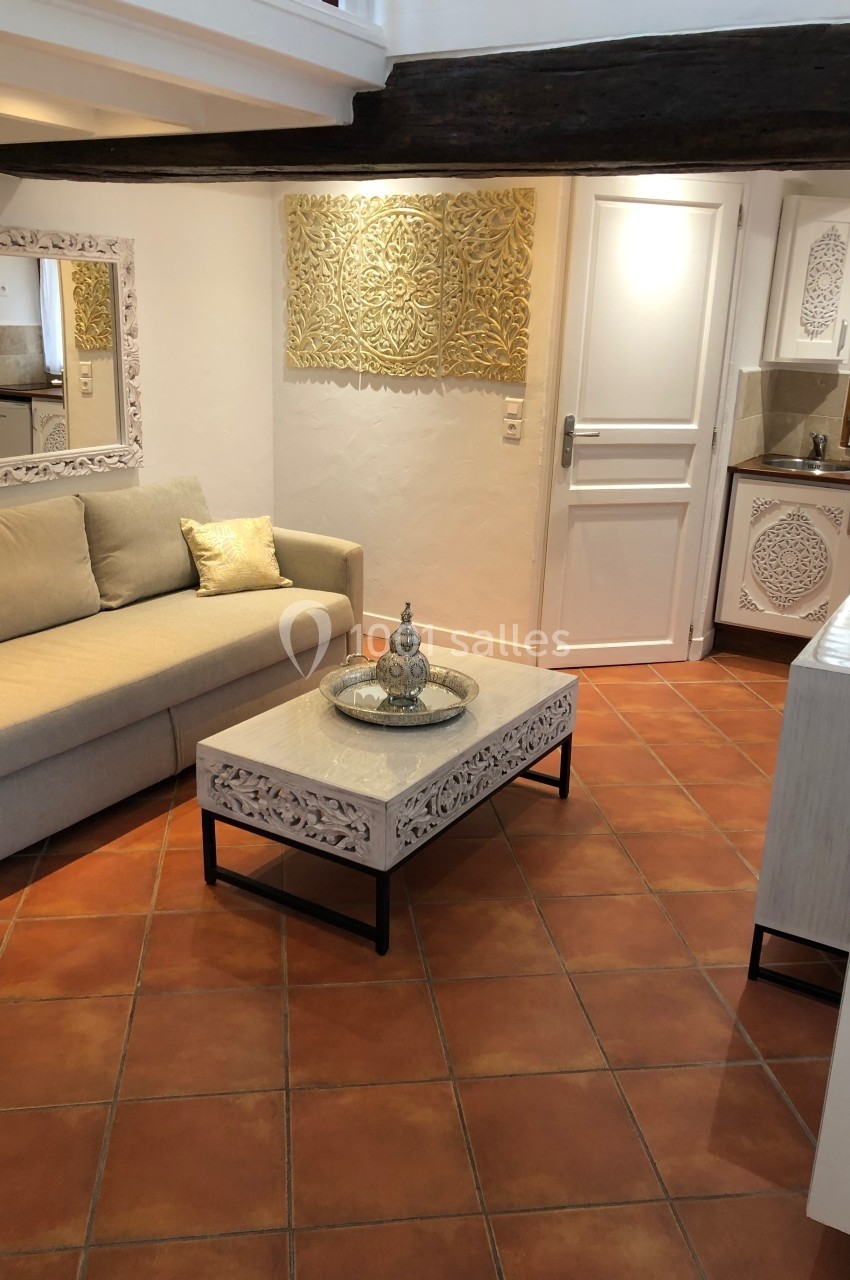 Location salle Beaulieu-sur-Loire (Loiret) - Domaine des Medards #7 Salon lumineux avec canapé beige, table basse sculptée, miroir assorti et cuisine ouverte en arrière-plan.