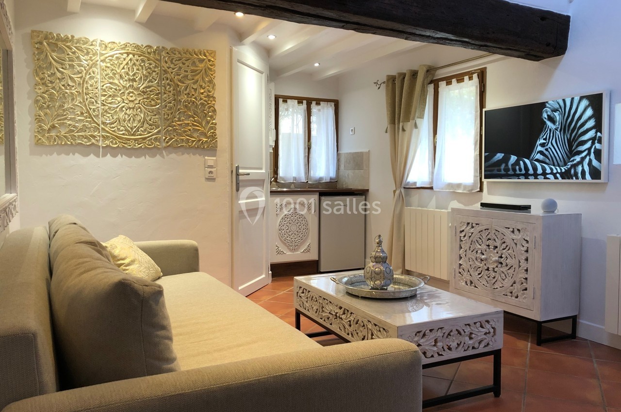 Location salle Beaulieu-sur-Loire (Loiret) - Domaine des Medards #8 Salon lumineux avec canapé beige, table basse sculptée, télévision murale et décoration en bois ajouré.