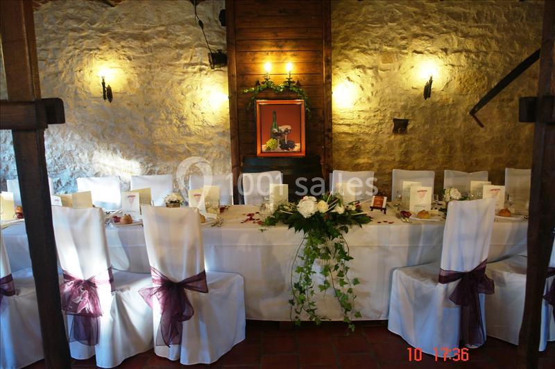 Salle décorée pour un repas festif avec une longue table dressée, chaises blanches ornées de nœuds bordeaux.
