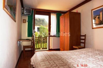 Chambre lumineuse avec deux lits simples, sol en carrelage, plafond en bois, et vue sur un jardin depuis une porte ouverte.