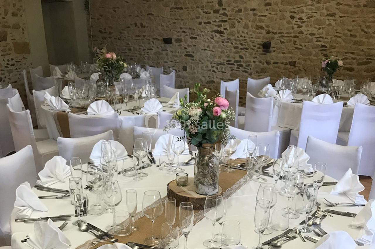 Salle de réception décorée avec des tables rondes dressées, nappes blanches et centres de table floraux.