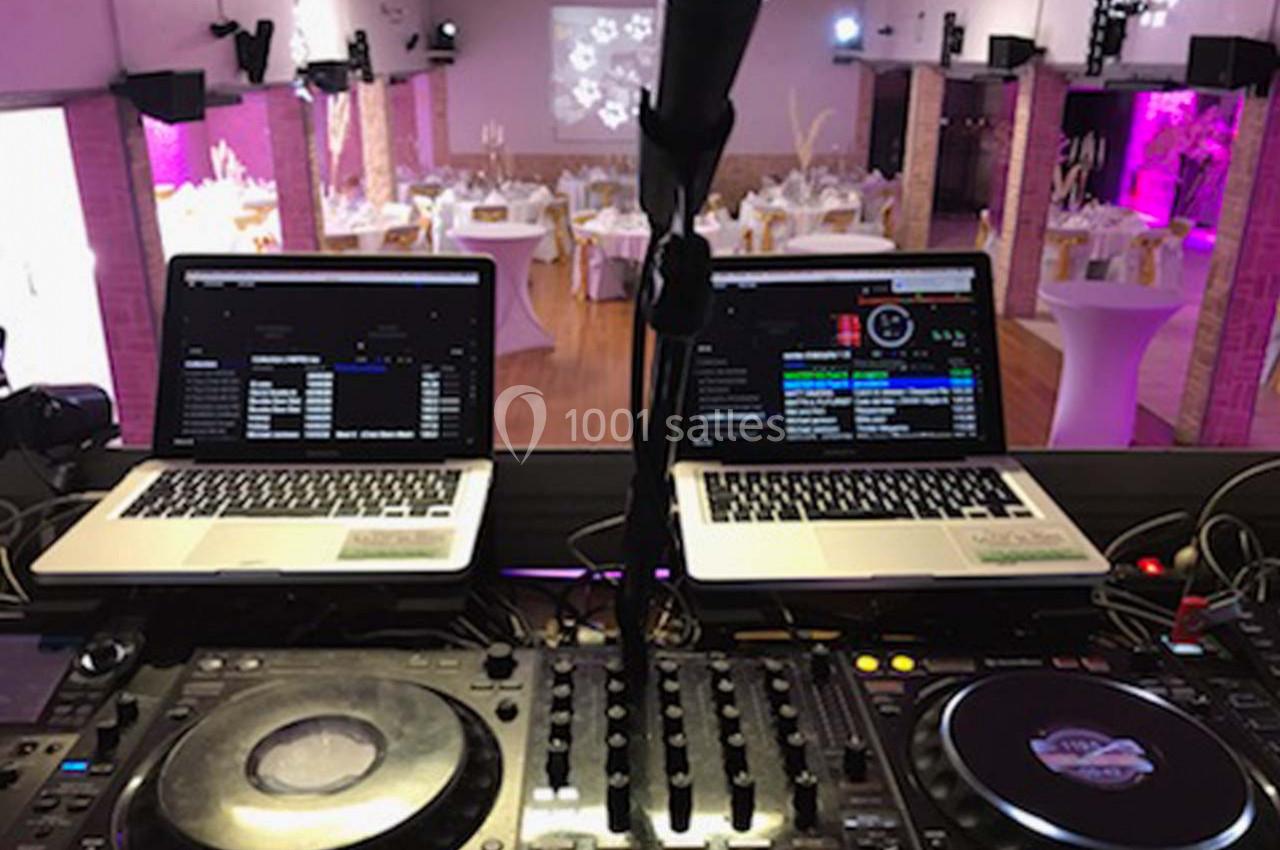 Poste de DJ avec deux ordinateurs portables, une table de mixage et une salle de réception décorée en arrière-plan.