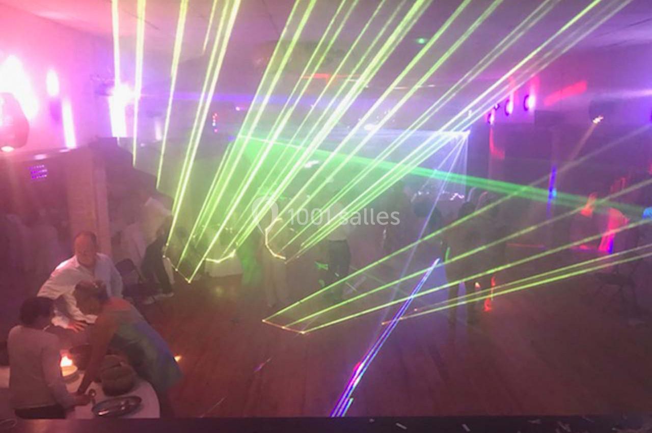 Des faisceaux laser colorés illuminent une salle sombre où des personnes dansent et discutent.