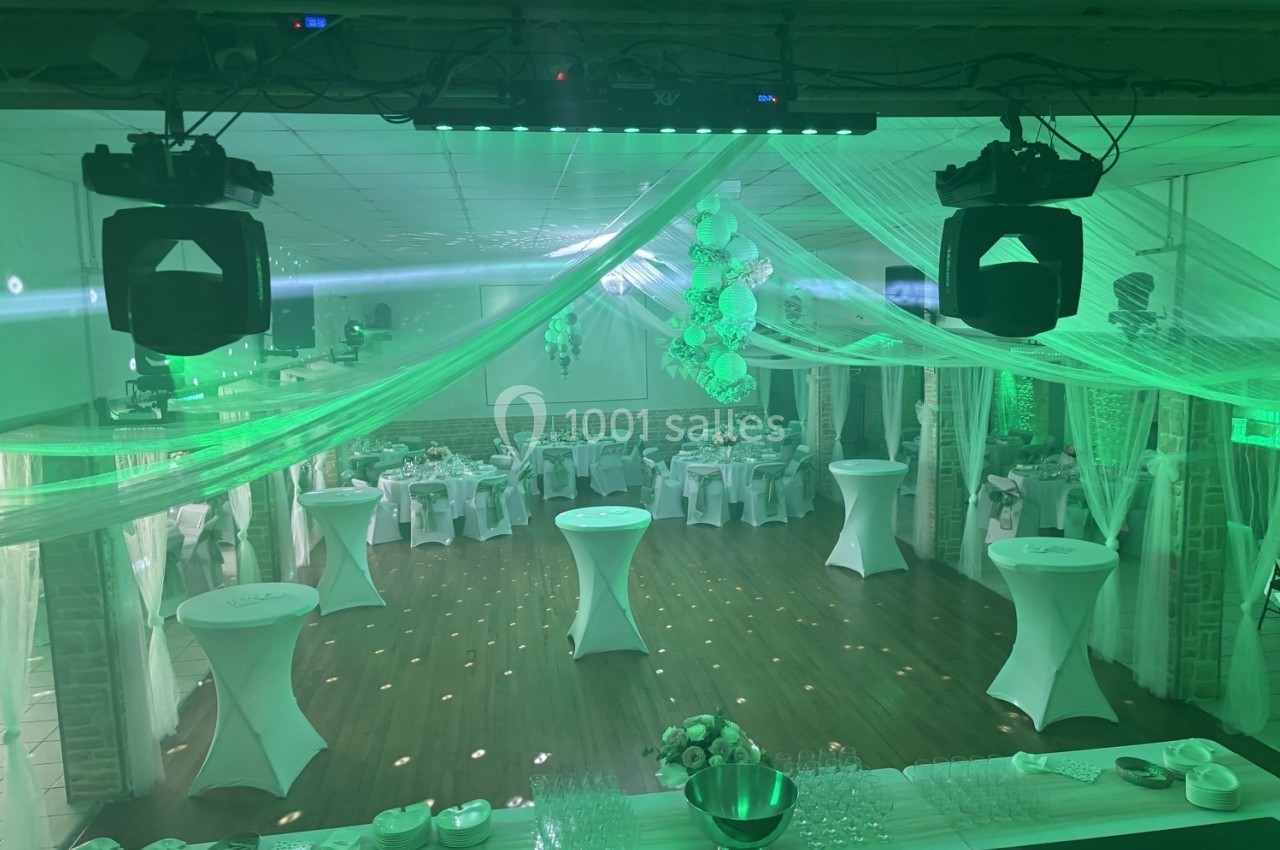 Salle de réception décorée avec des nappes blanches, des tables hautes et un éclairage vert diffus.