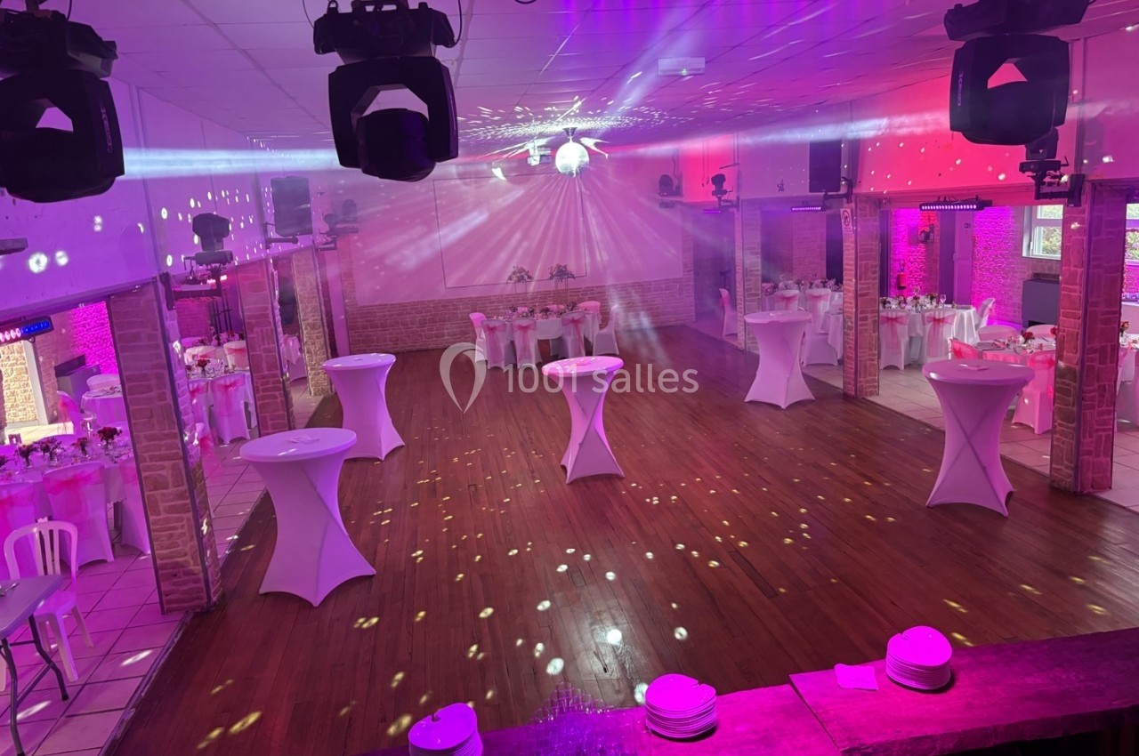 Salle de réception décorée avec des tables hautes et des jeux de lumière, prête pour un événement festif.