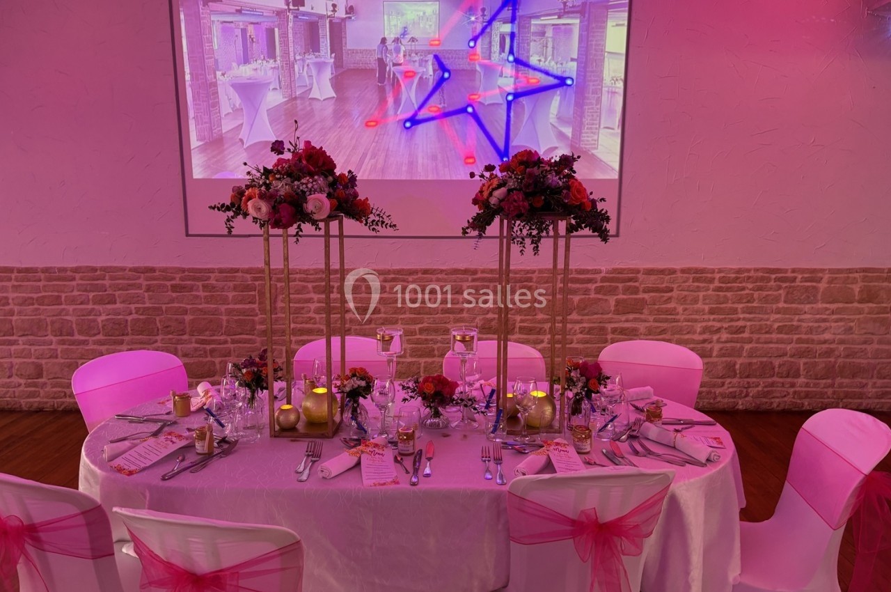 Table décorée pour un événement avec nappes blanches, chaises ornées de rubans roses et centre de table floral.