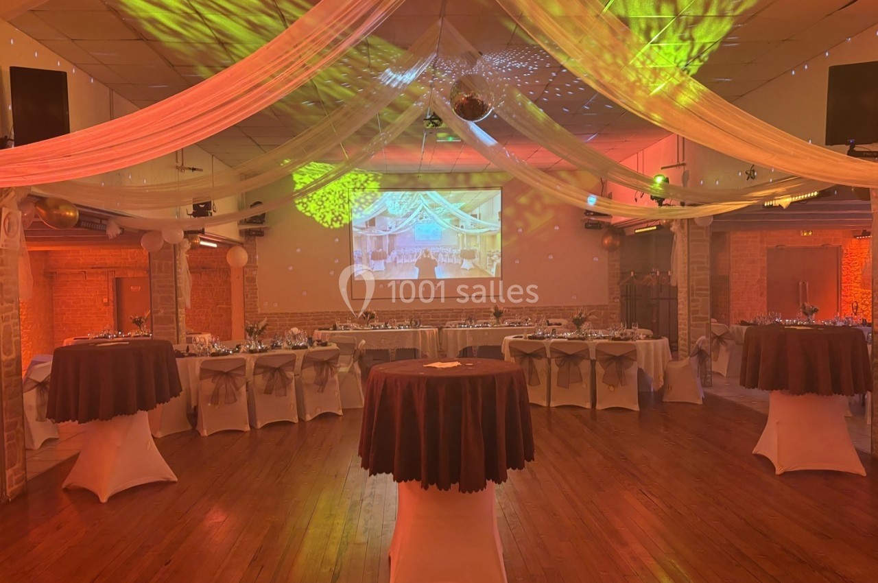 Salle de réception décorée avec des tables dressées, des drapés suspendus et un éclairage coloré.