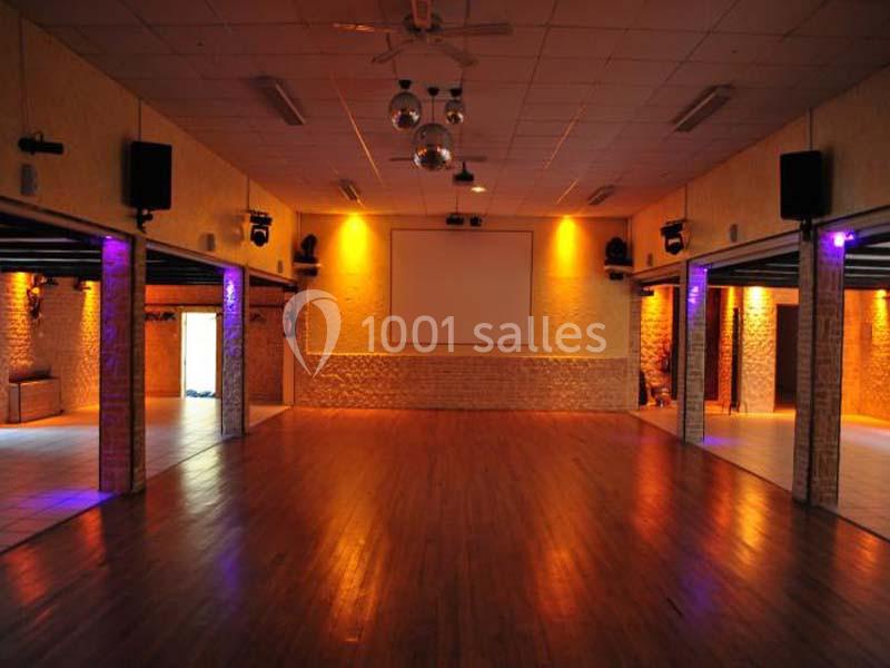 Salle spacieuse avec parquet, murs en pierre et éclairage tamisé, équipée d'un écran et de projecteurs au plafond.