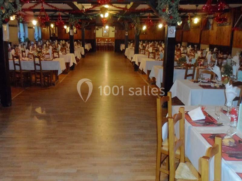 Salle de réception décorée pour un événement, avec des tables dressées et des chaises en bois disposées en rangées.
