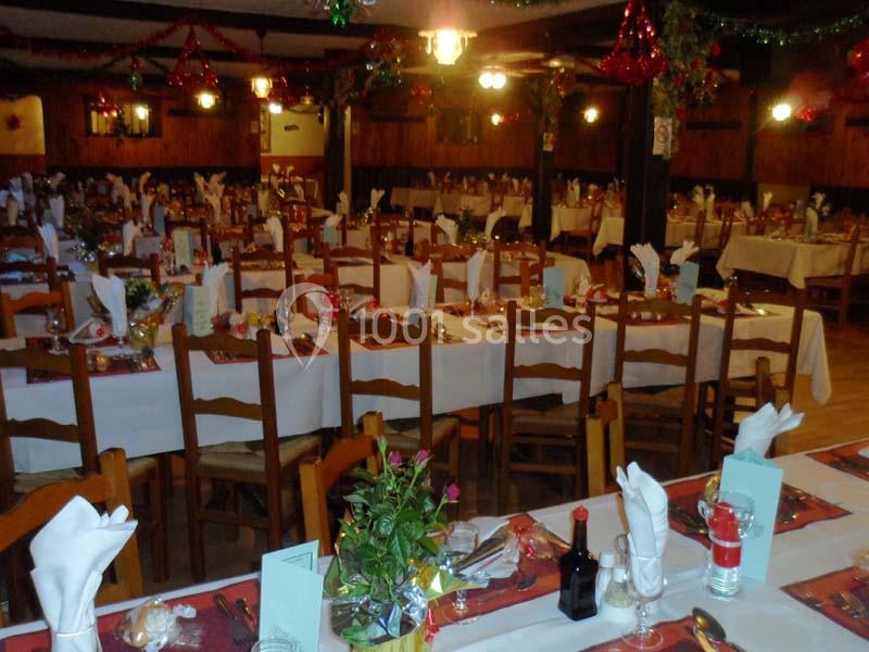 Salle de réception décorée avec des tables dressées pour un repas, ornées de nappes blanches et de décorations festives.