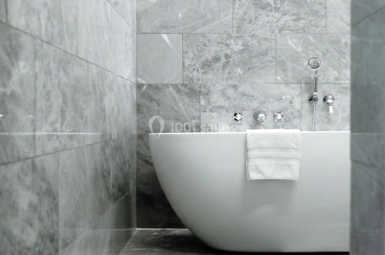 Salle de bain moderne avec baignoire blanche et murs en marbre gris.
