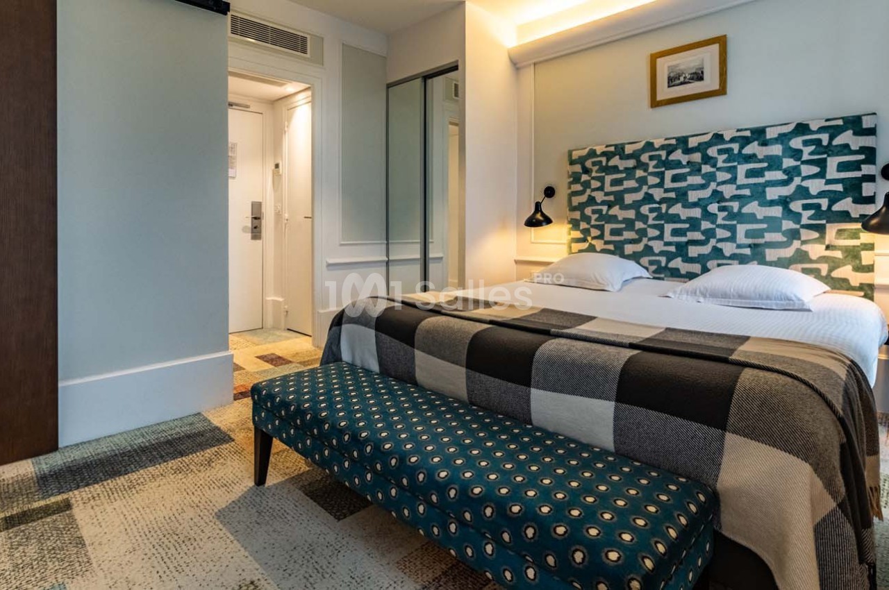 Chambre d'hôtel moderne avec lit double, tête de lit géométrique, banc rembourré et éclairage mural.