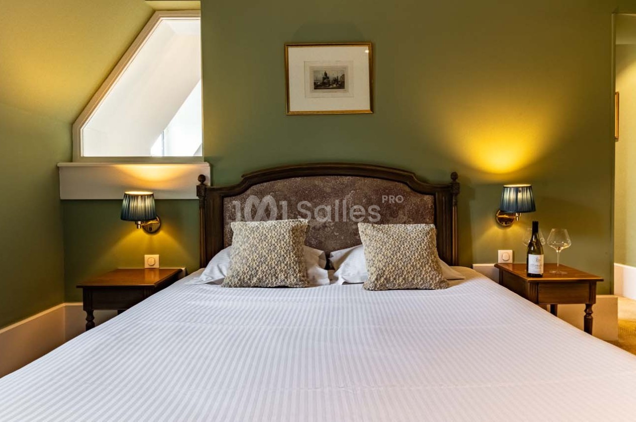 Lit double avec tête de lit en bois, deux tables de chevet, lampes allumées et mur vert en arrière-plan.