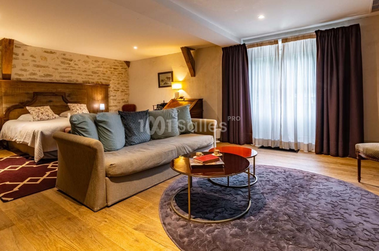 Chambre spacieuse avec lit double, canapé, table basse et grande fenêtre avec rideaux, décorée dans un style chaleureux.