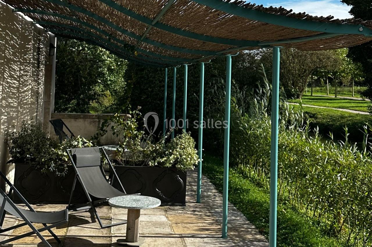 Terrasse ombragée avec pergola en canisses, chaises longues, table basse et vue sur un jardin verdoyant.