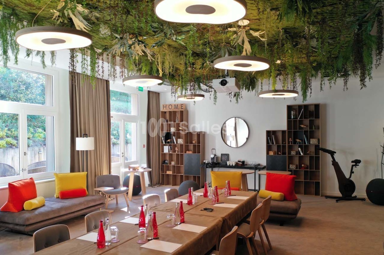 Salle lumineuse avec une grande table dressée, plafond végétalisé, canapés colorés et équipements de détente.
