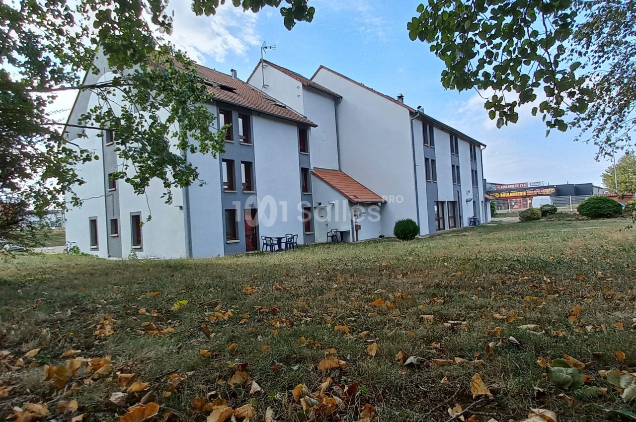 Bâtiment résidentiel blanc à plusieurs étages entouré d'un espace vert avec des arbres et des feuilles au sol.