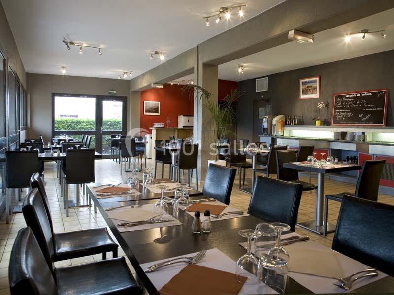 Salle de restaurant moderne avec tables dressées, chaises noires, éclairage doux et tableau noir au mur.