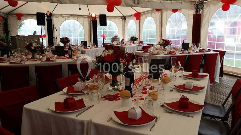 Tables décorées avec nappes blanches et accents rouges dans une tente pour un événement festif.