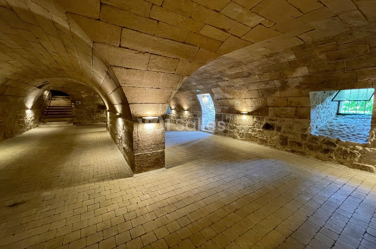 Voûtes en pierre éclairées, avec un sol pavé et des ouvertures laissant entrer la lumière naturelle.