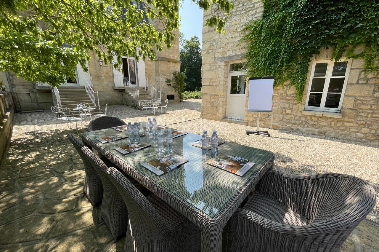 Table en rotin avec documents et bouteilles d'eau, installée dans une cour pavée entourée de bâtiments en pierre.