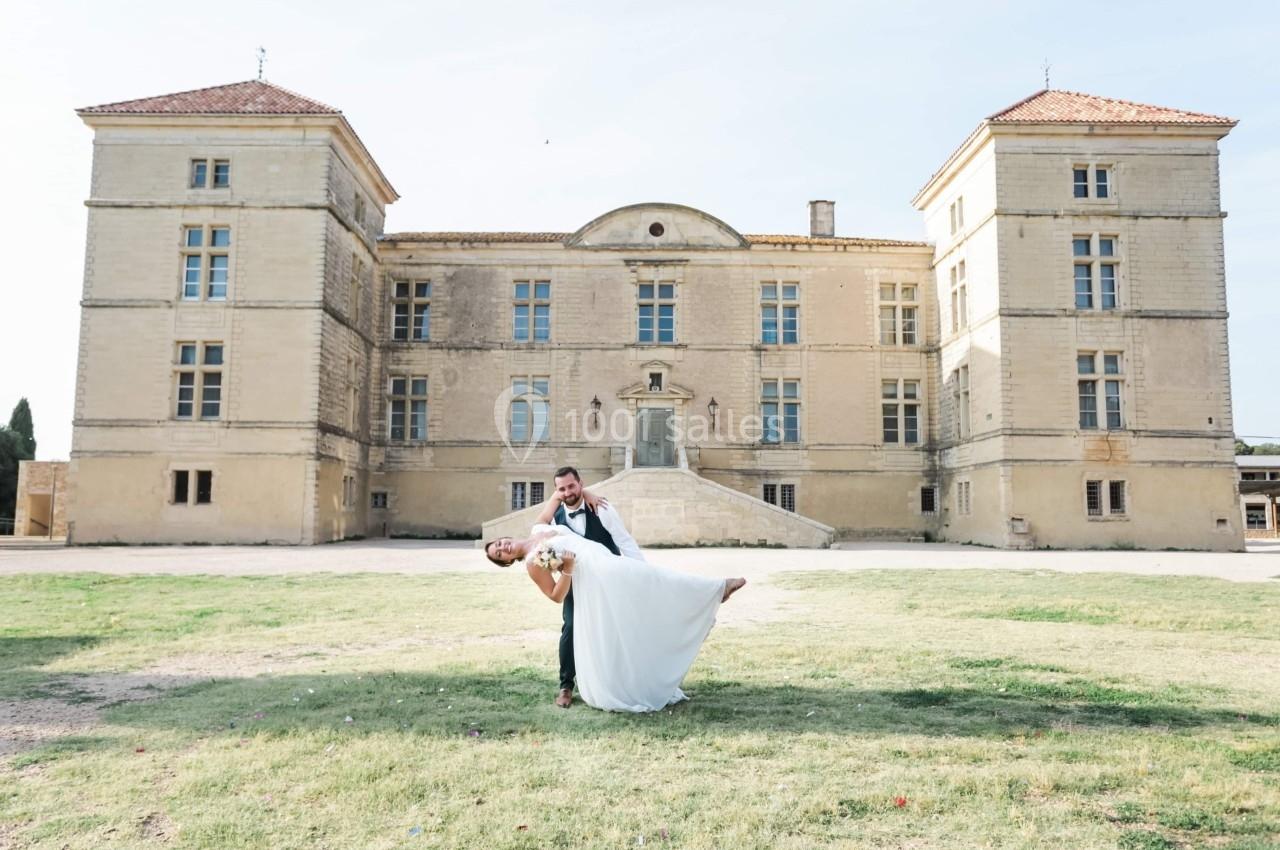 Un couple de mariés pose devant un château ancien, l'homme inclinant la femme dans une danse élégante.