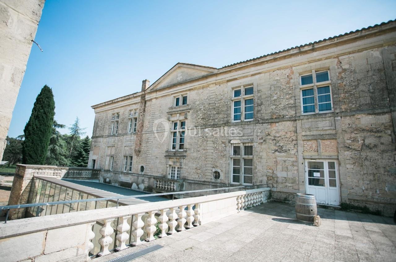 Façade en pierre d'un bâtiment ancien avec balustrade, fenêtres à carreaux et ciel dégagé en arrière-plan.