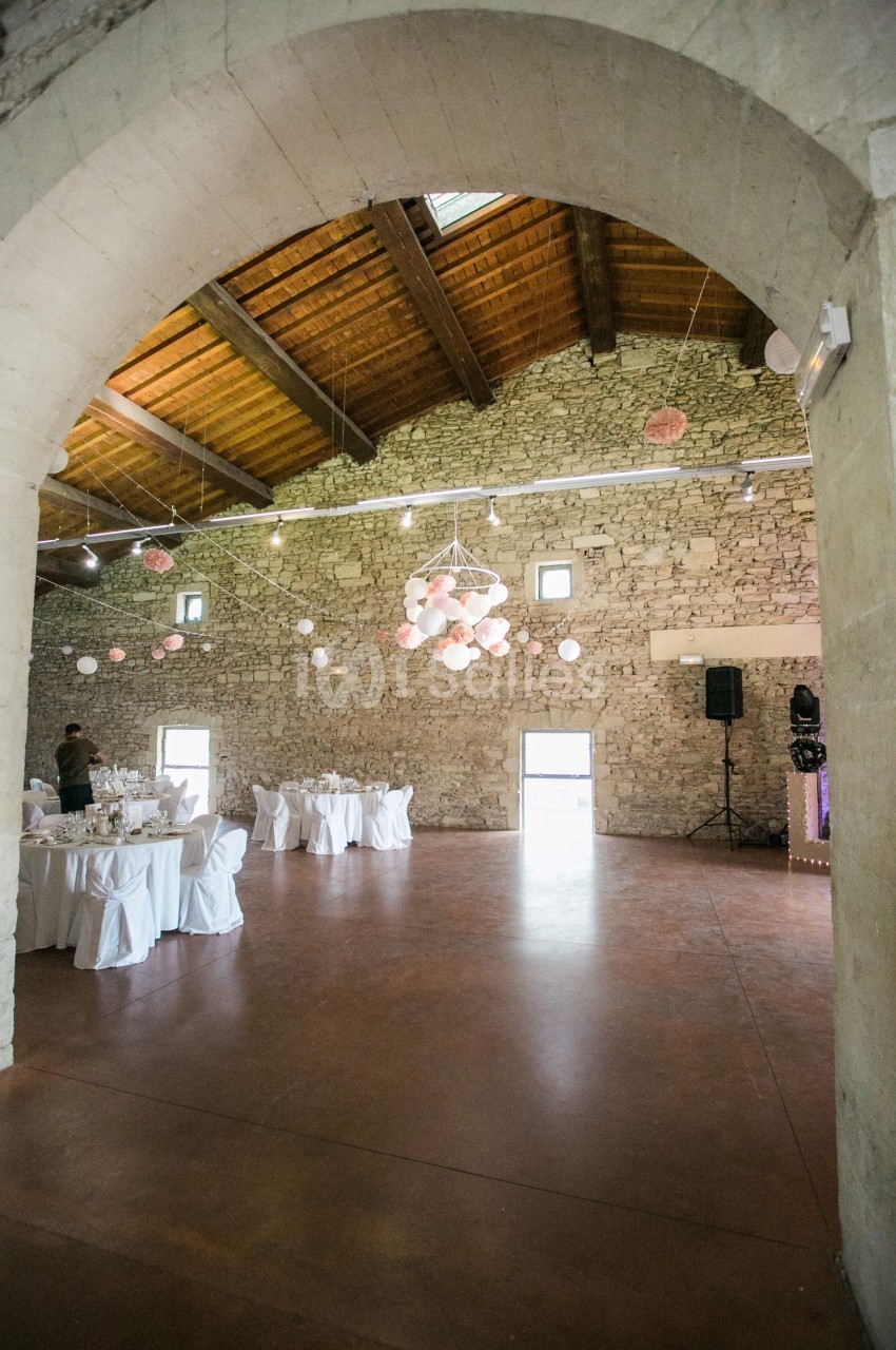 Salle en pierre avec plafond en bois, décorée de guirlandes lumineuses et de lanternes, tables dressées pour un événement.