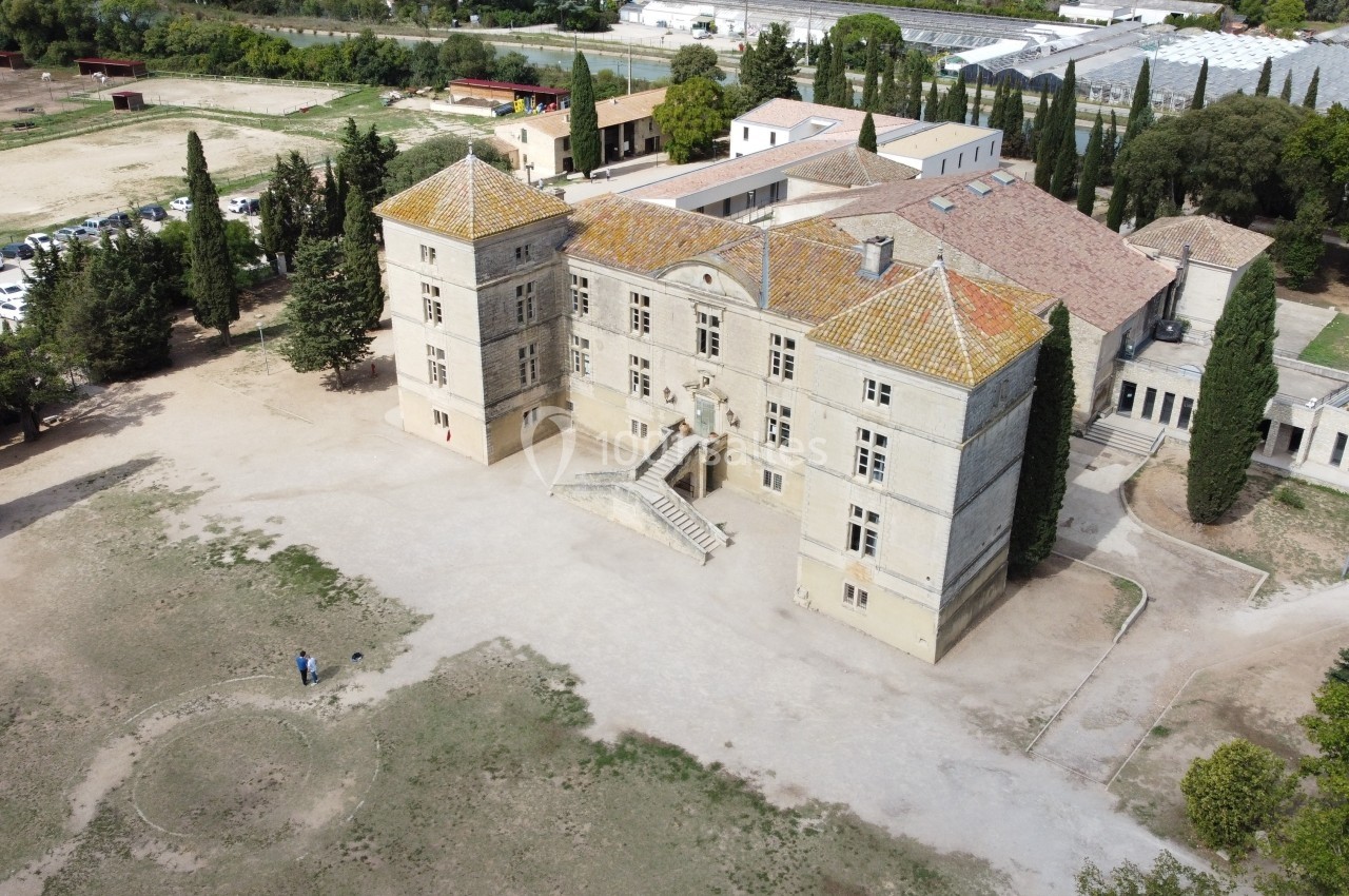 Vue aérienne d'un château ancien entouré d'arbres, avec des bâtiments annexes et un parking à proximité.