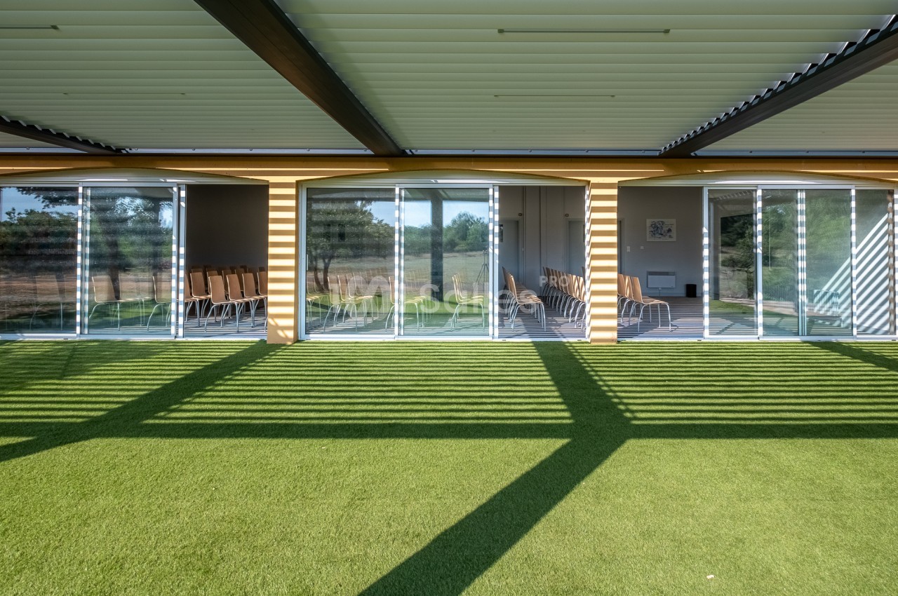 Salle vitrée donnant sur un espace extérieur avec pelouse synthétique, ombragée par une pergola.