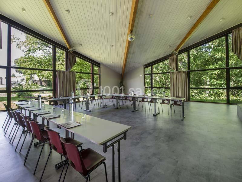 Salle de réunion lumineuse avec de grandes baies vitrées, des tables disposées en U et des chaises rouges.